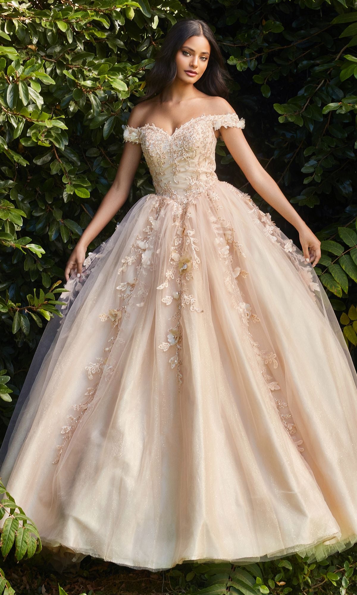 A woman stands outdoors amid green foliage, wearing the Off-Shoulder Long Sweetheart Prom Ball Gown CD0185 in blush pink with floral-lace appliques and a full, layered skirt.